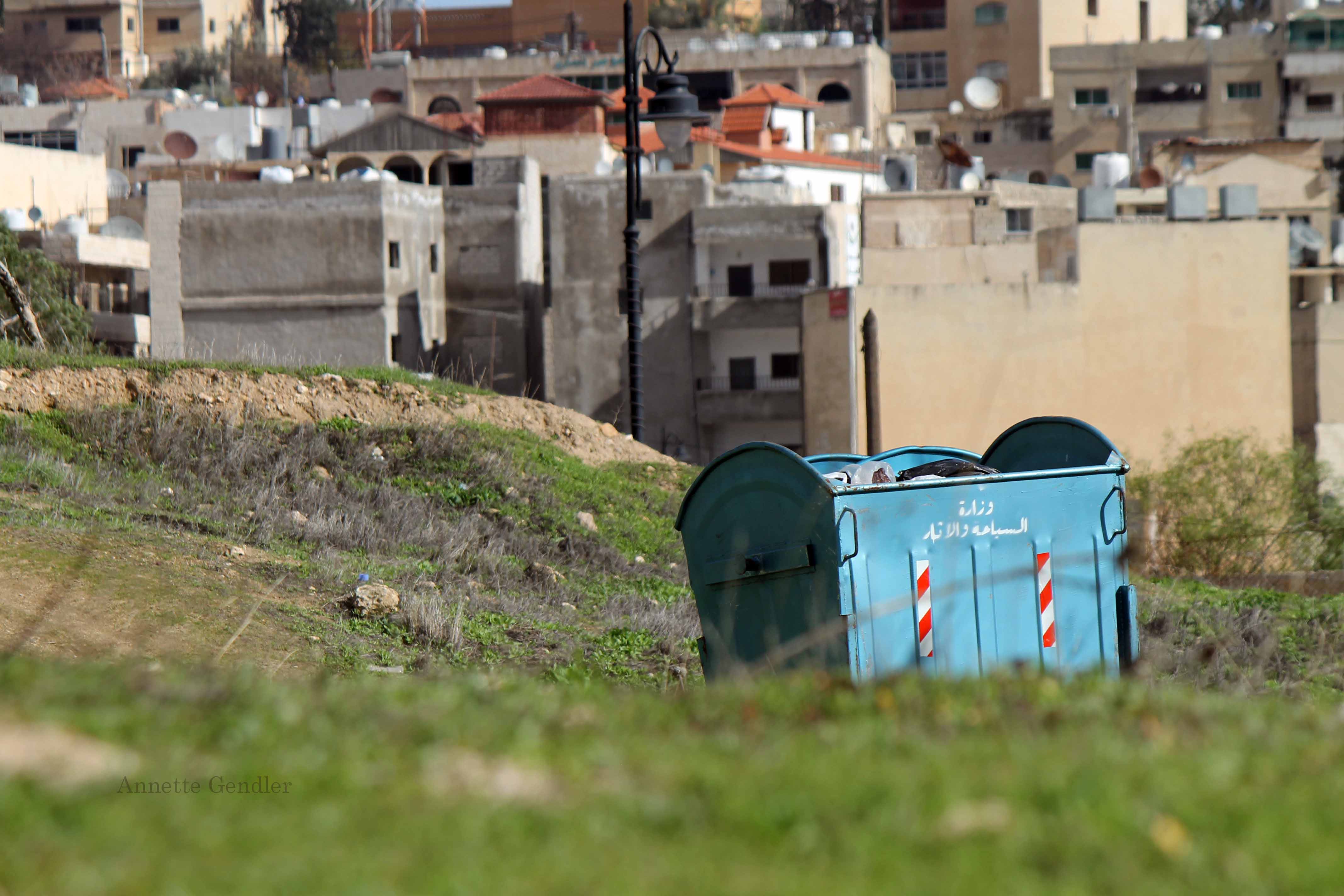 garbage dumpster in field with buildings behind it in Jerash, Jordan