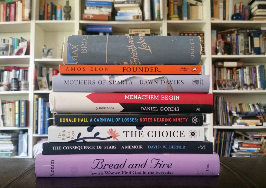 Pile of books to be read in front of a crowded bookshelf