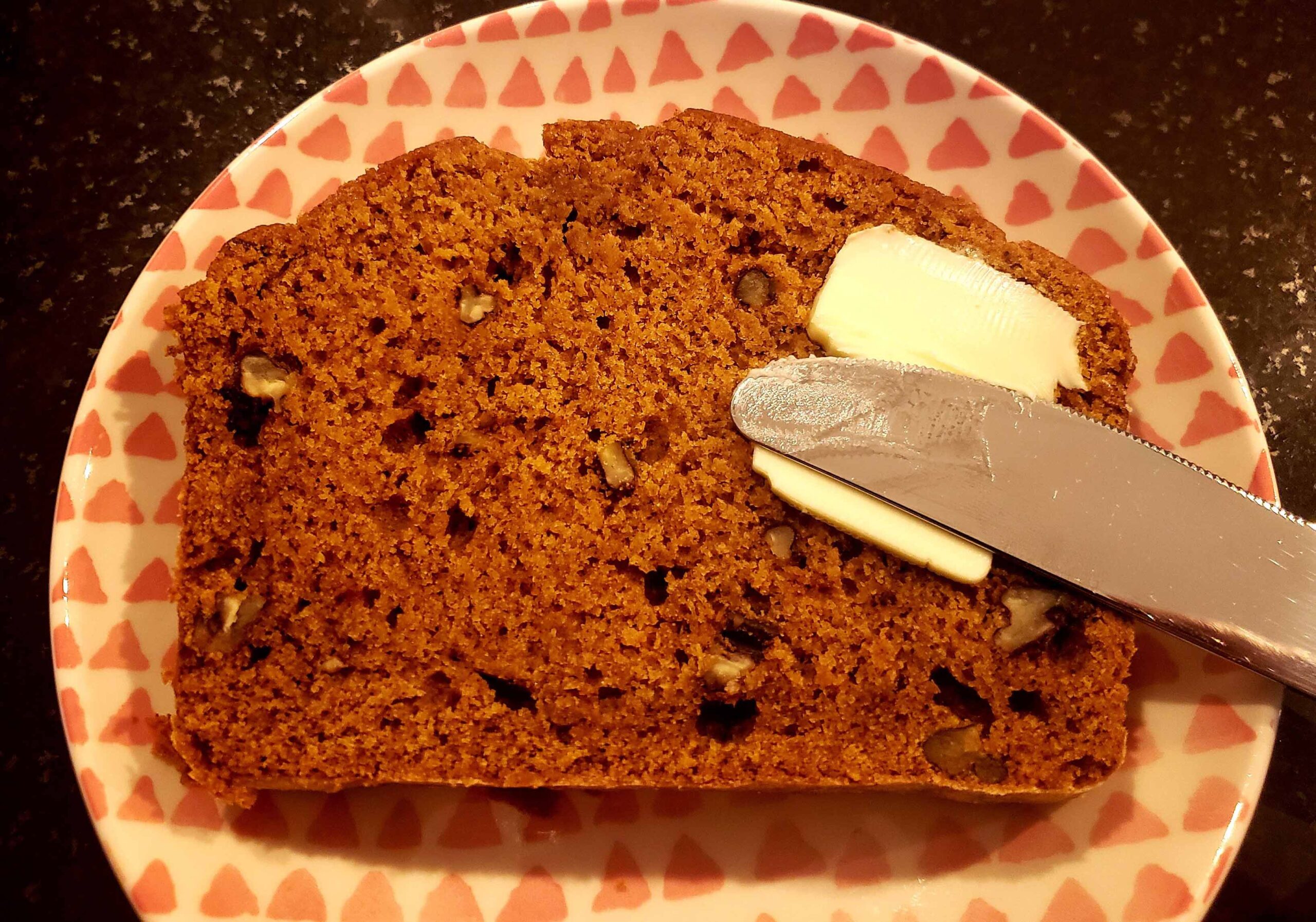 slide of pumpkin bread on red patterned plate and knife with butter smeared on