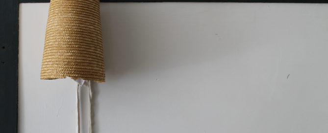 Shaker straw bonnet handing on a dark peg on white wall