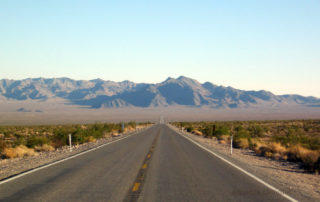 Empty, straight paved road in Nevada leading to the mountains in the distance