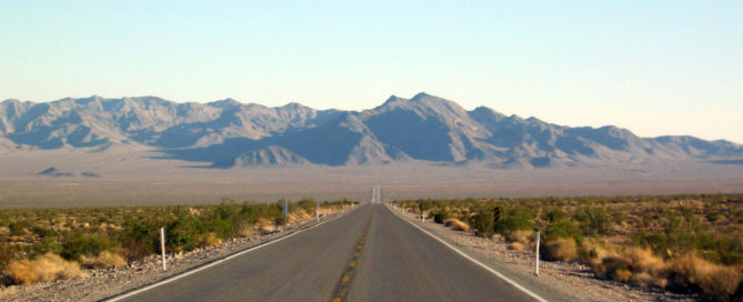 Empty, straight paved road in Nevada leading to the mountains in the distance
