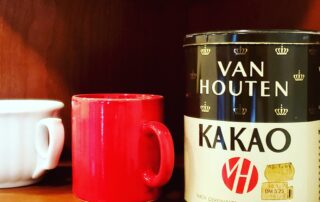 Van Houten cocoa tin on brown shelf with red and white mugs next to it